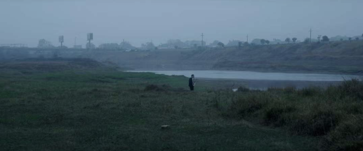 A lone figure on a grassy riverbank