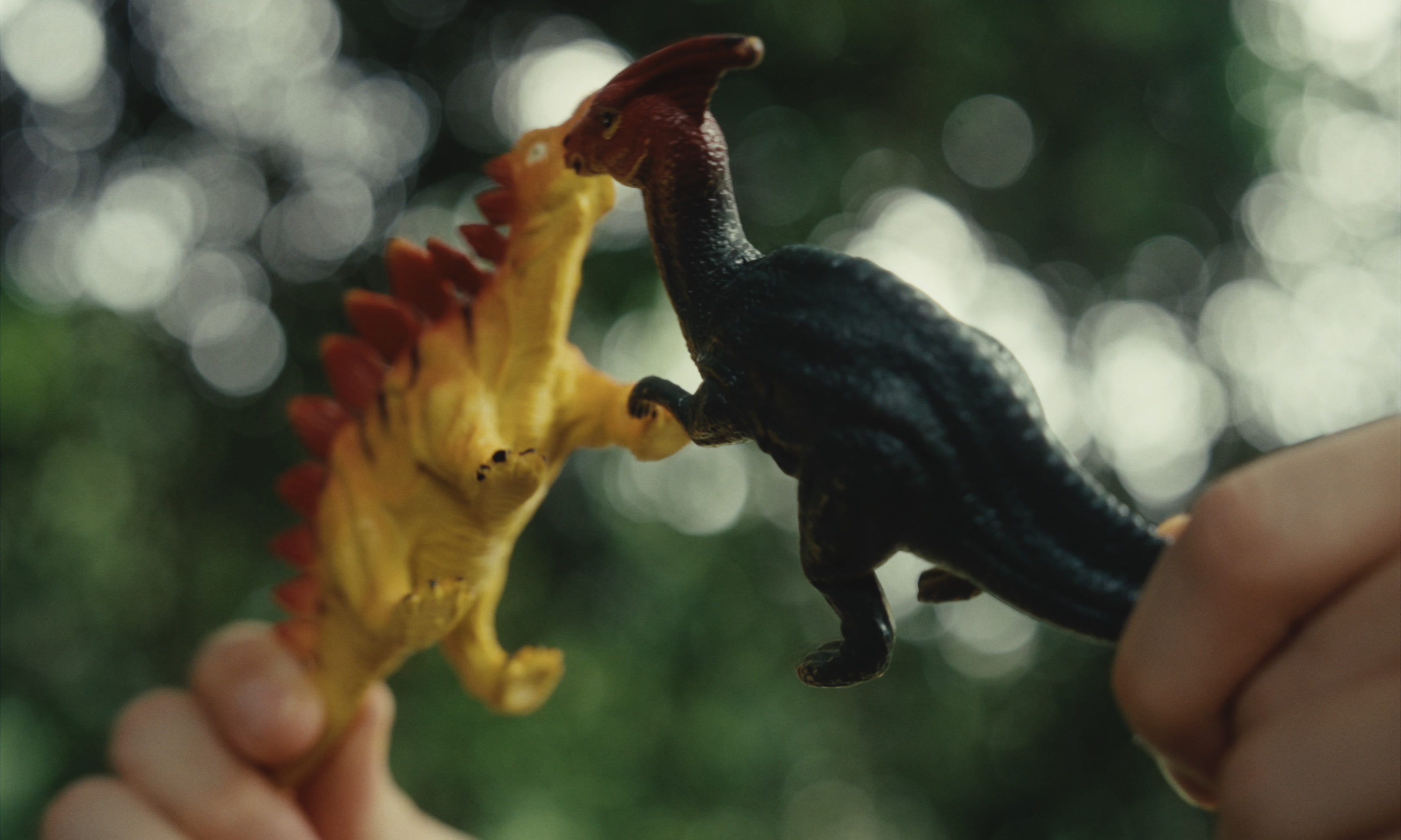 Two toy dinosaurs held beneath trees