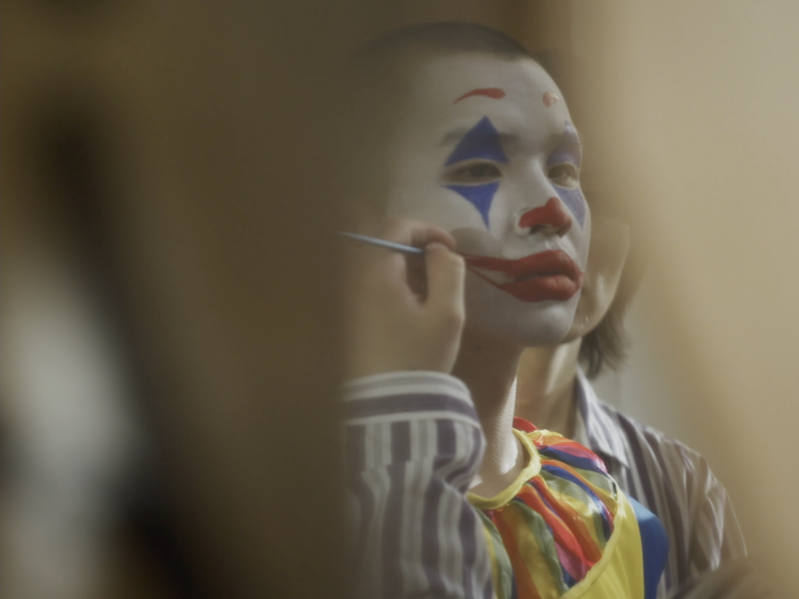 A clown applying makeup in a mirror